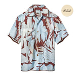 A short-sleeve button-up shirt in light blue and brown, with an abstract, wavy camouflage-style pattern. It has two front chest pockets and a pointed collar.