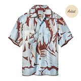 A short-sleeve button-up shirt in light blue and brown, with an abstract, wavy camouflage-style pattern. It has two front chest pockets and a pointed collar.