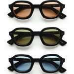 Three variations of the Lesca Lunetier X Tombolo Lenses where all feature a black lens frame and different lens colors (From top to bottom: Coral, Charcoal, and Azure) with front-facing product imagery where the glasses appear above one another on a white background.