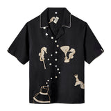 Casual black short-sleeve button-up shirt with white piping and embroidered beige seahorses holding barware, including a martini glass, cocktail shaker, and bottle. White buttons run diagonally down the front, resembling rising bubbles.