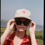 woman holds sunglasses wearing cap