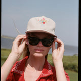 woman holds sunglasses wearing cap
