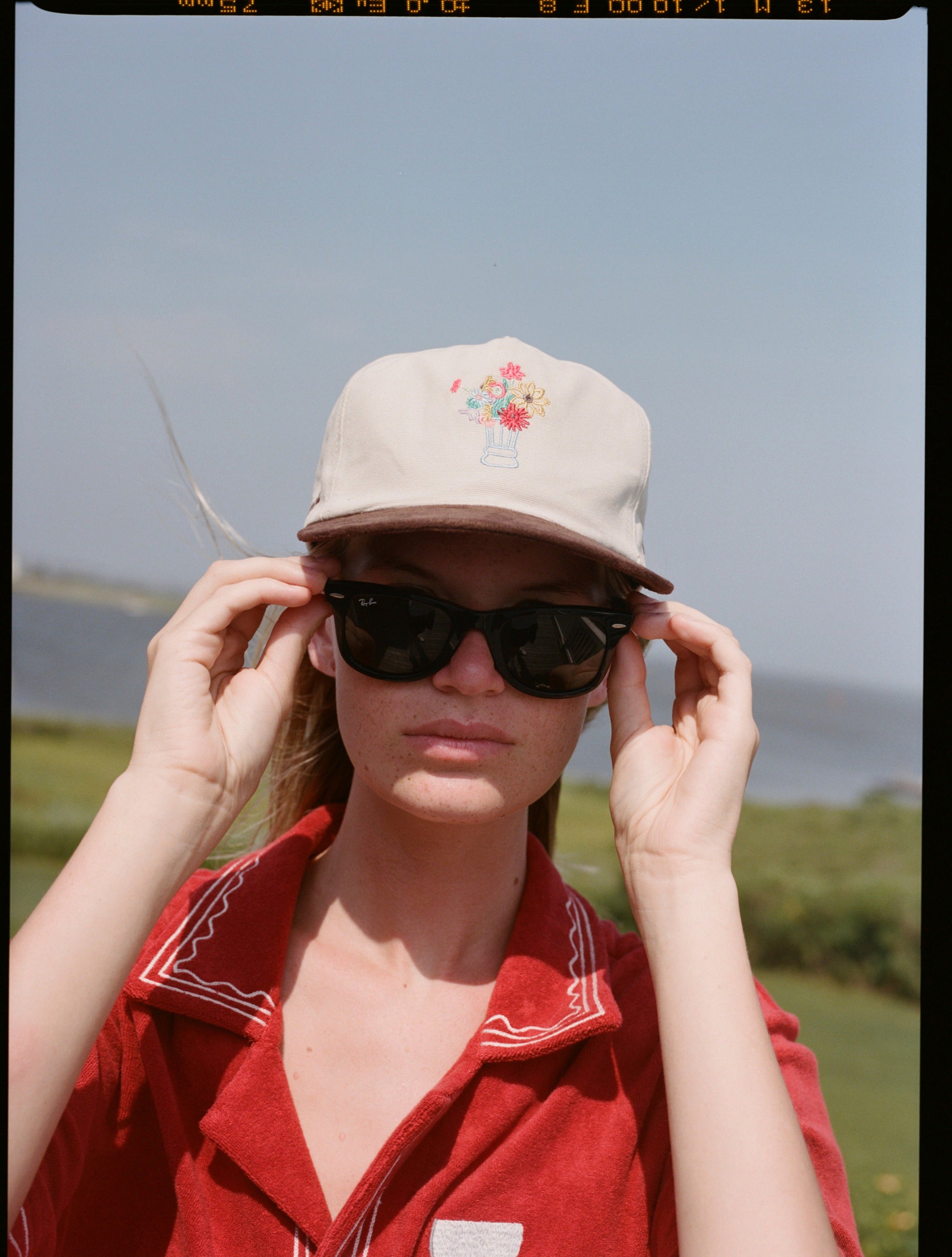 woman holds sunglasses wearing cap