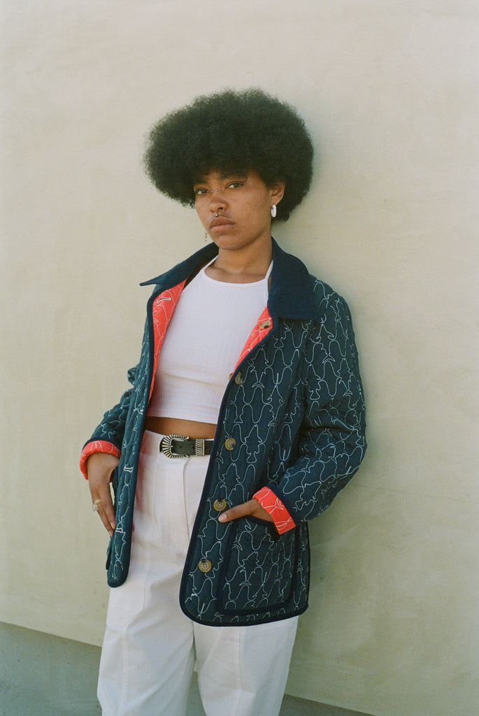 Woman leans against wall in unbuttoned jacket
