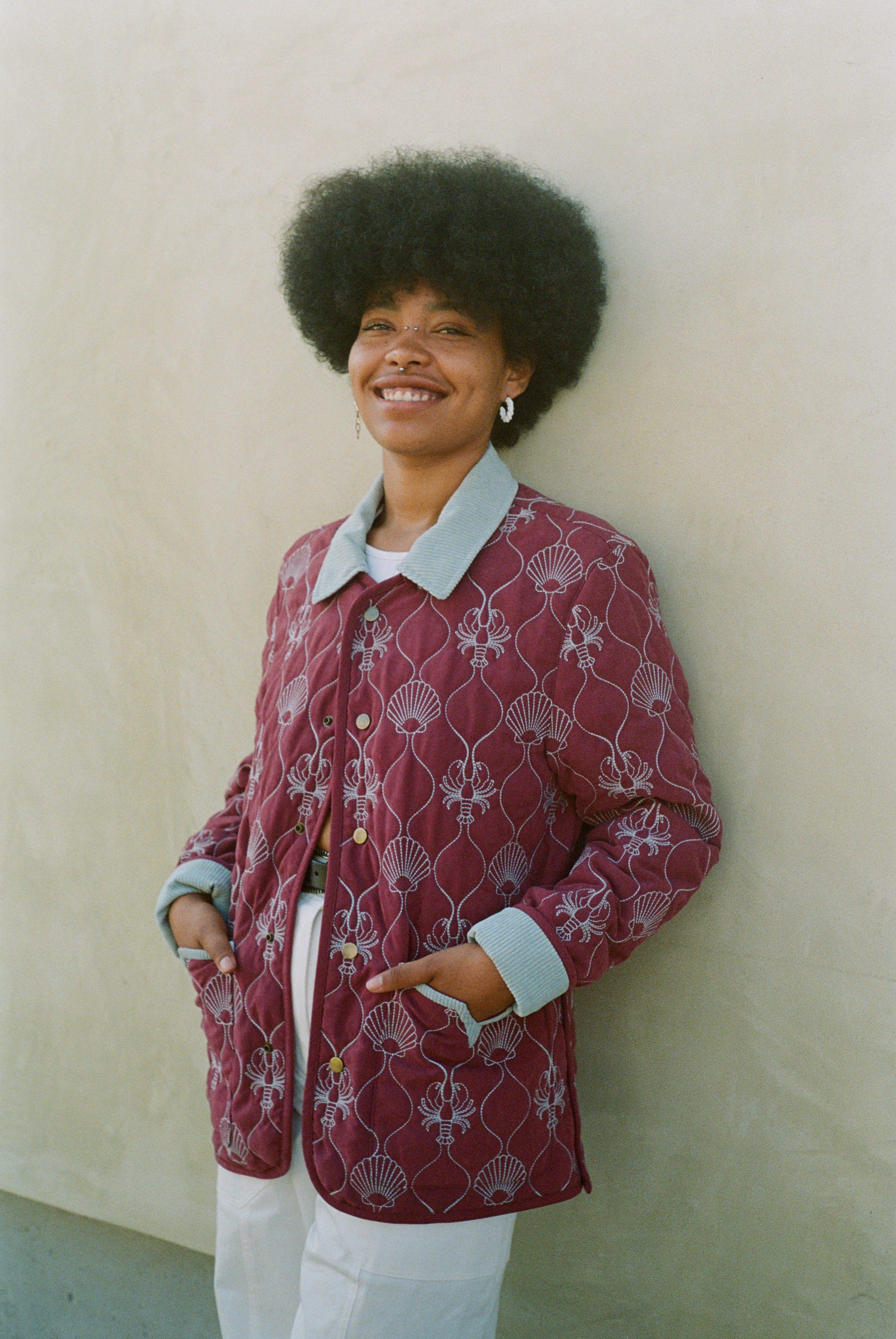 Woman leans against wall with hands in jacket pockets