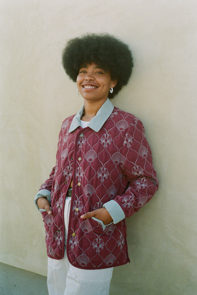 Woman leans against wall with hands in jacket pockets