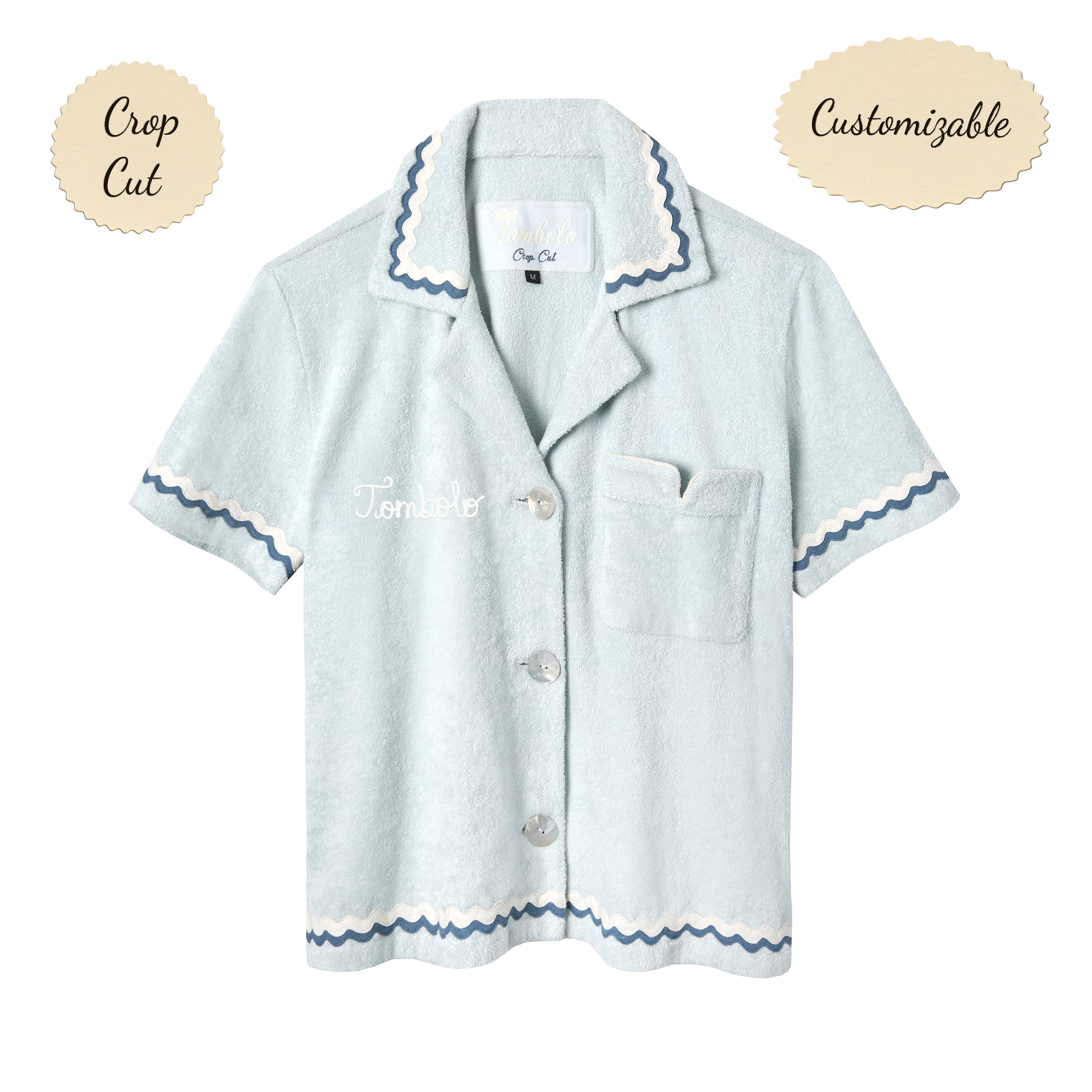 Light blue terrycloth crop-cut shirt with short sleeves and scalloped trim in navy and white. Features a front chest pocket with flap, white embroidered 'Tombolo' text on the chest, and mother-of-pearl buttons.