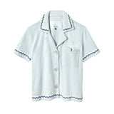 Light blue terrycloth crop-cut shirt with short sleeves and scalloped trim in navy and white. Features a front chest pocket with flap, white embroidered 'Tombolo' text on the chest, and mother-of-pearl buttons.