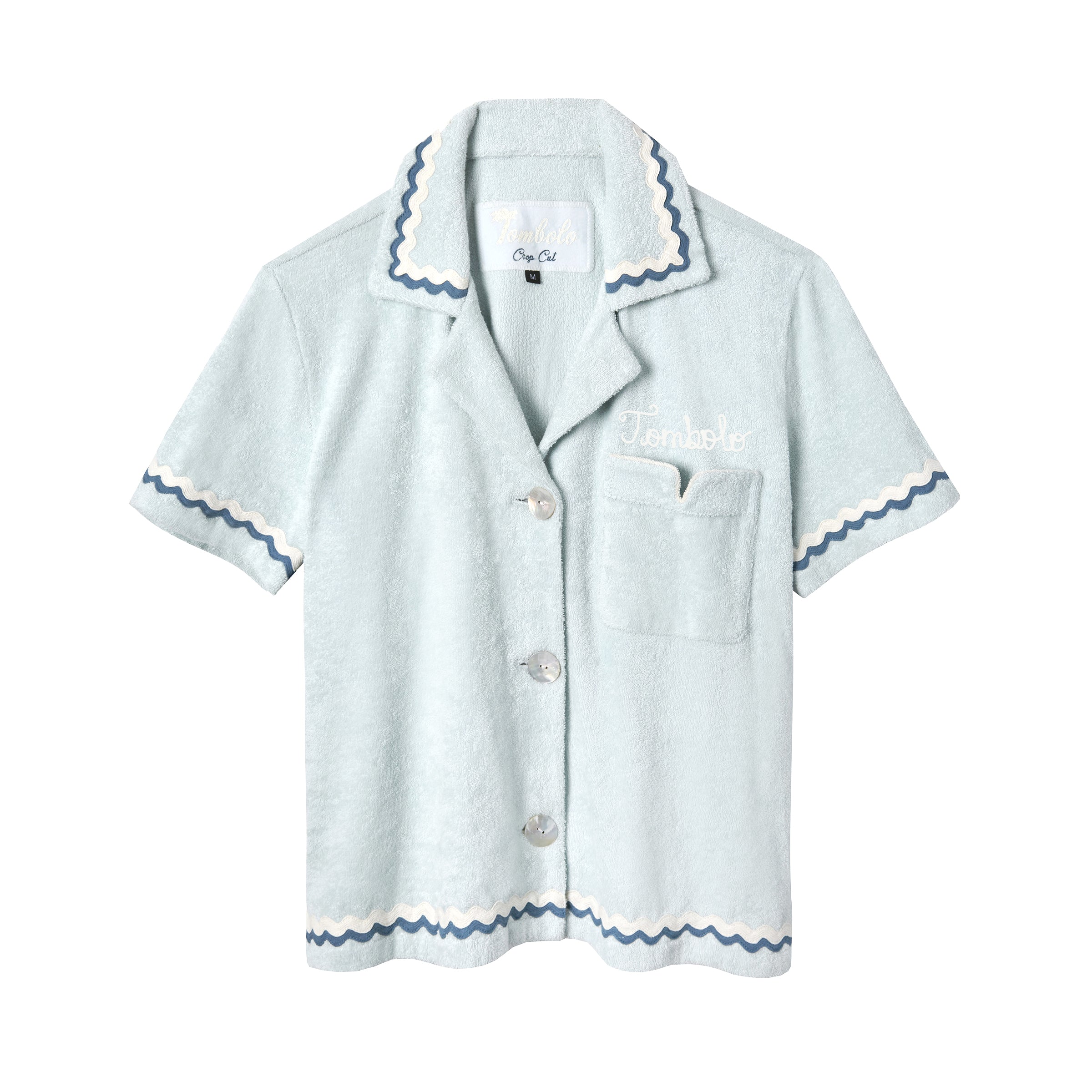Light blue terrycloth crop-cut shirt with short sleeves and scalloped trim in navy and white. Features a front chest pocket with flap, white embroidered 'Tombolo' text on the chest, and mother-of-pearl buttons.