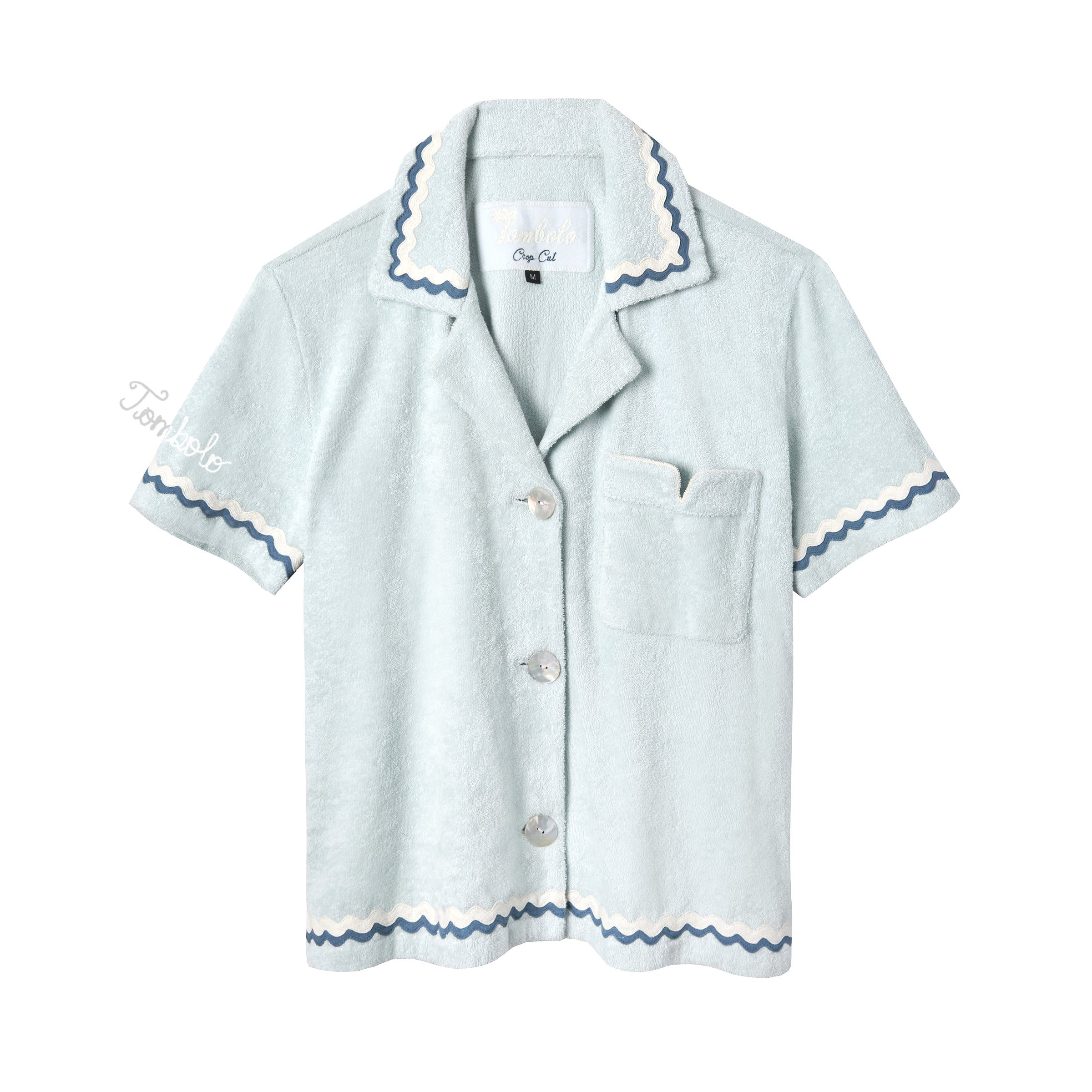 Light blue terrycloth crop-cut shirt with short sleeves and scalloped trim in navy and white. Features a front chest pocket with flap, white embroidered 'Tombolo' text on the sleeve, and mother-of-pearl buttons.