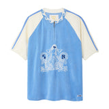 A light blue and cream raglan-style short-sleeve top with a half-zip neckline, featuring a white graphic print of a mermaid and the letters 'S B' on the front, set against a plain white background.