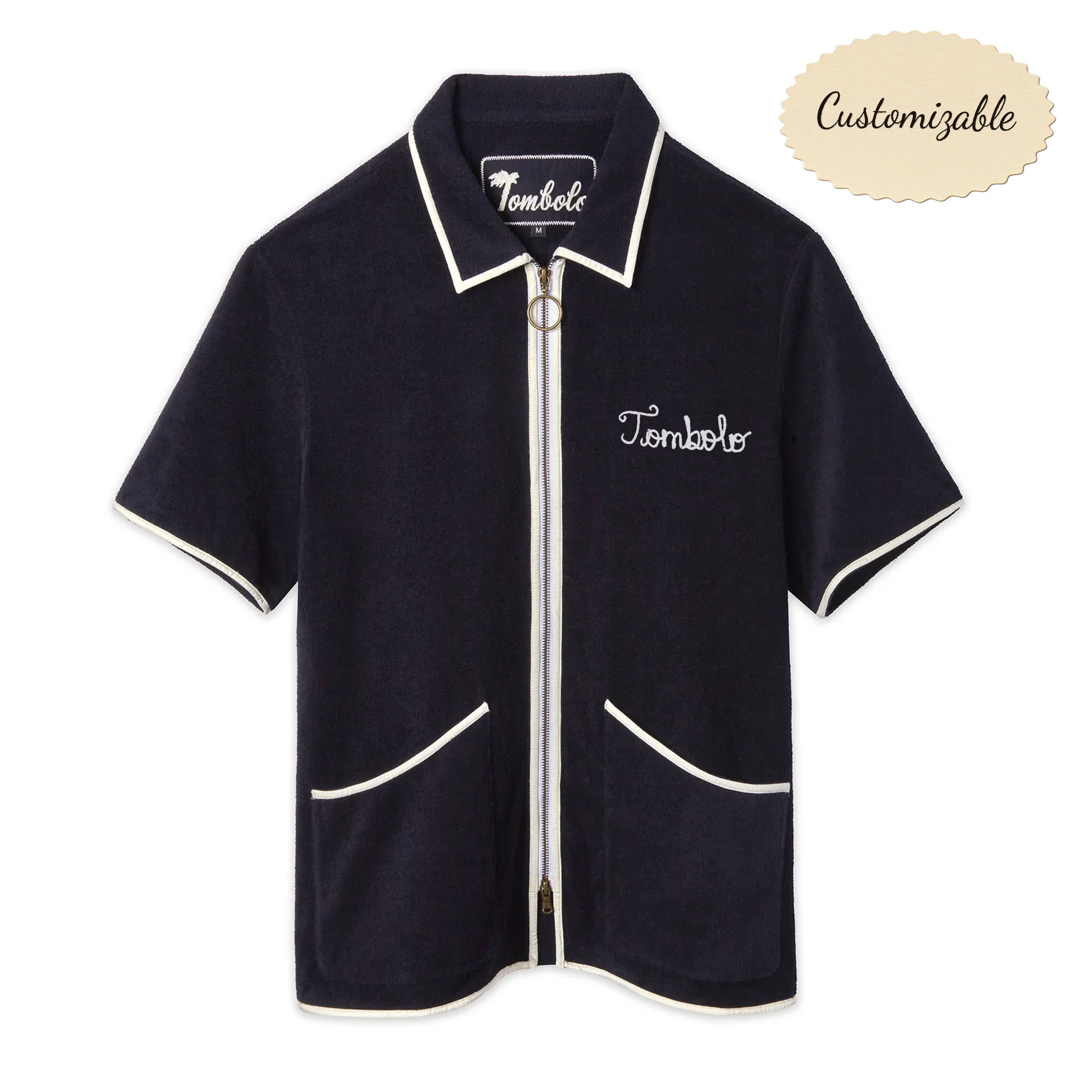 Navy terry zip-up shirt with white piping along the collar, sleeves, pockets, and zipper. Features an O-ring zipper pull and white 'Tombolo' embroidery on the chest.