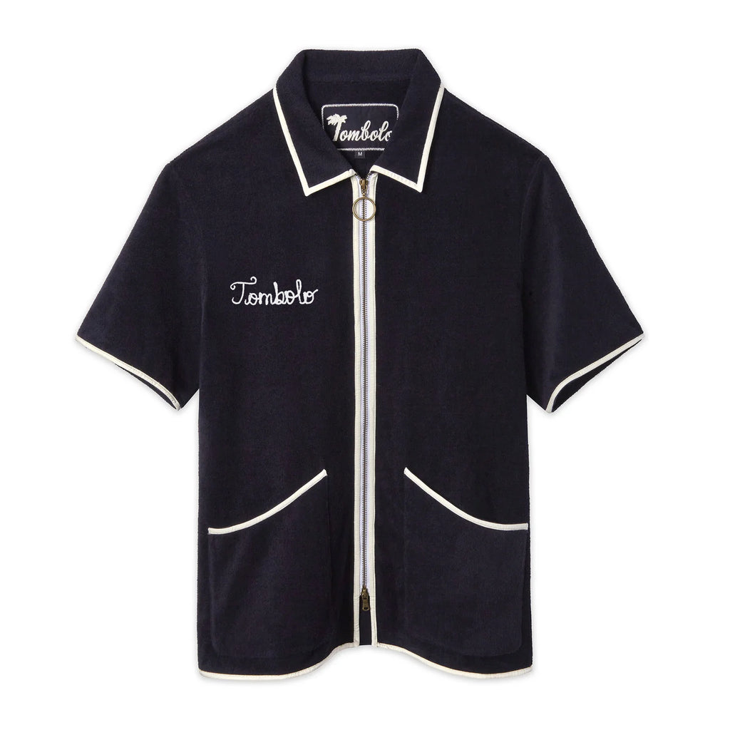  Navy terry zip-up shirt with white piping along the collar, sleeves, pockets, and zipper. Features an O-ring zipper pull and white 'Tombolo' embroidery on the chest.