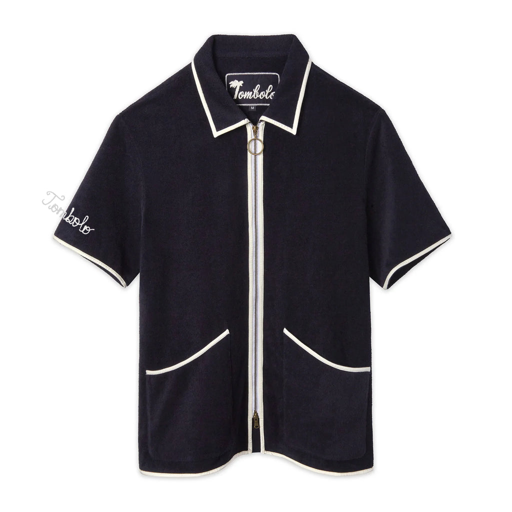 Navy terry zip-up shirt with white piping along the collar, sleeves, pockets, and zipper. Features an O-ring zipper pull and white 'Tombolo' embroidery on the sleeve.