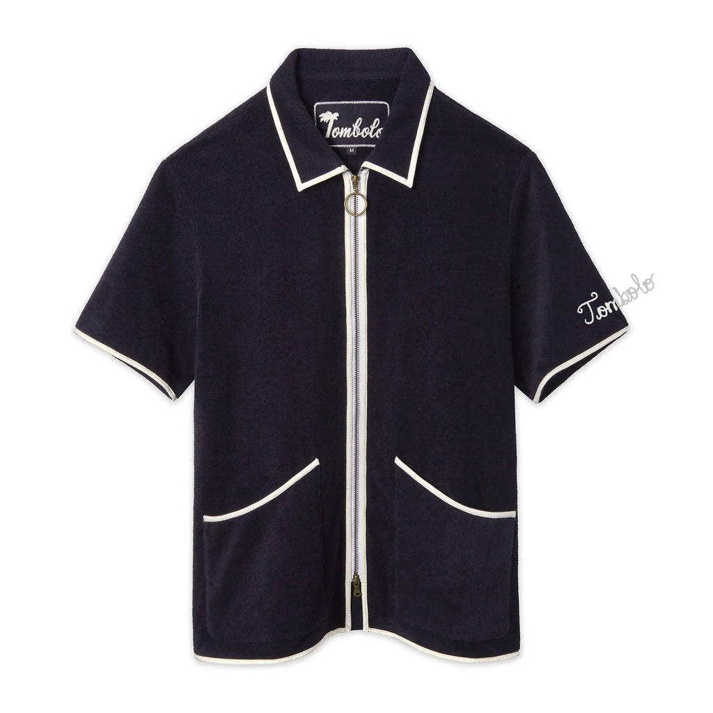 Navy terry zip-up shirt with white piping along the collar, sleeves, pockets, and zipper. Features an O-ring zipper pull and white 'Tombolo' embroidery on the sleeve.