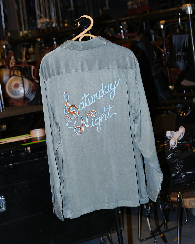 A green button-up shirt featuring a 'Saturday Night' chain-stitched in metallic thread on the back.