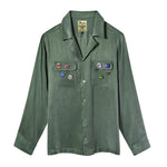 Olive green long-sleeve button-up shirt with two chest pockets and assorted SNL pin badges.