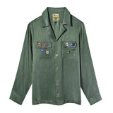Olive green long-sleeve button-up shirt with two chest pockets and assorted SNL pin badges.
