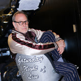SNL costume designer, Tom Broecker, is seen sitting in the SNL studio, while wearing the 'SNL" Souvenir Jacket and Navy Easy Going Striped pants. 
