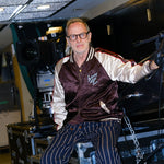 SNL costume designer, Tom Broecker, is seen sitting in the SNL studio, while wearing the 'SNL" Souvenir Jacket and Navy Easy Going Striped pants. 