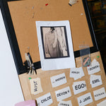 Corkboard with pinned reference photo and labeled name cards arranged in a grid.