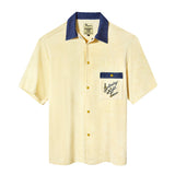 A pale yellow terry cloth short-sleeved shirt with mid-wash denim details, featuring a 'Saturday Night Live' logo on the chest pocket and custom snap buttons.