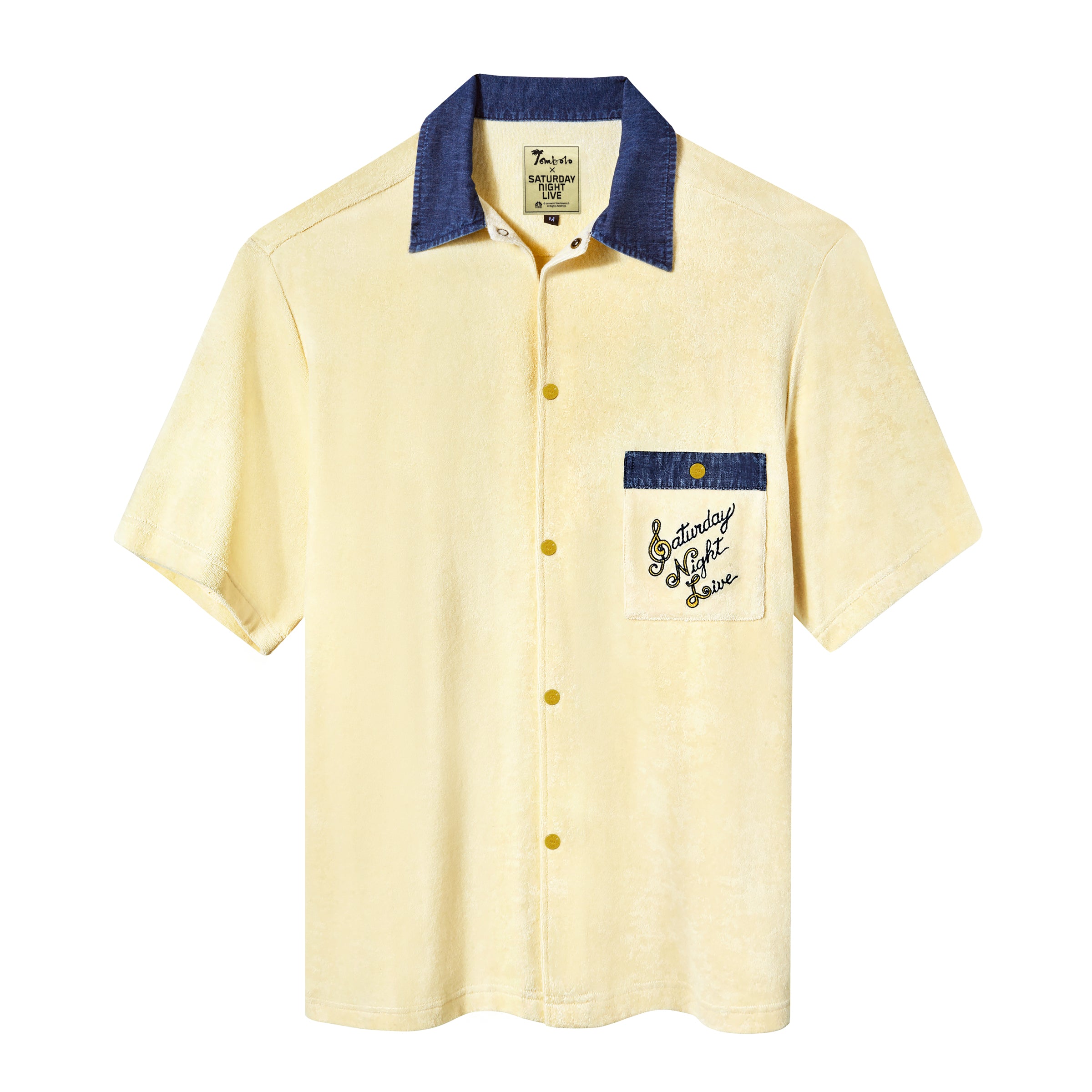A pale yellow terry cloth short-sleeved shirt with mid-wash denim details, featuring a 'Saturday Night Live' logo on the chest pocket and custom snap buttons.