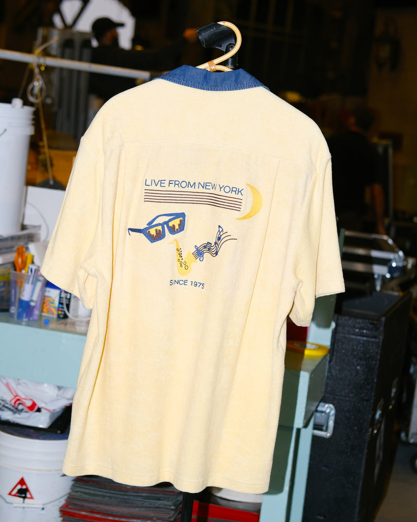 Backside of pale yellow terry cloth cabana shirt, featuring original artwork chain-stitched on the back, paying homage to SNL’s rich history of musical guests and the promise of a crescent moon rising over the greatest city in the world on a Saturday night.