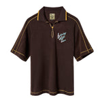 A brown Saturday Night Live x Tombolo polo shirt with yellow overlock stitching and a chain-stitched 'Saturday Night Live' logo on the left chest.