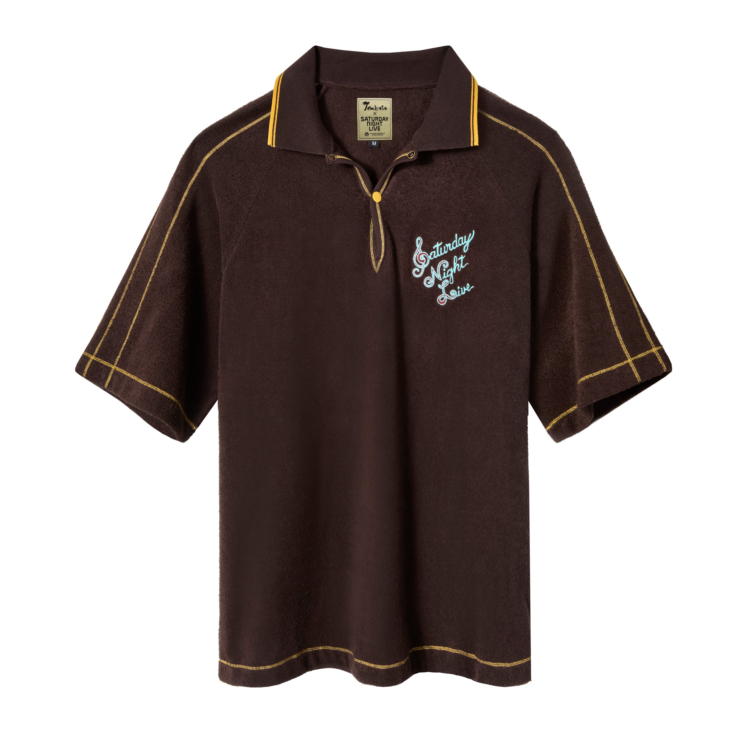 A brown Saturday Night Live x Tombolo polo shirt with yellow overlock stitching and a chain-stitched 'Saturday Night Live' logo on the left chest.