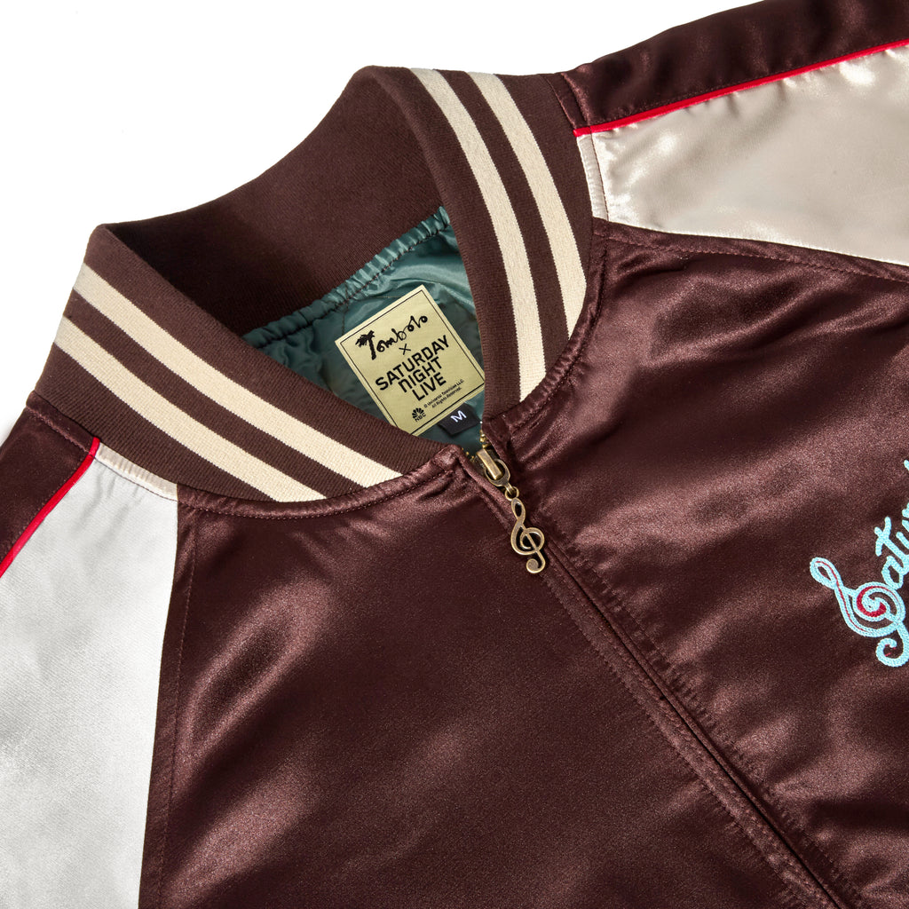Close-up of the collar of 'SNL' Souvenir Jacket, with a musical note zipper pull and an interior label with 'Tombolo x Saturday Night Live' stitched. 