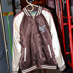 A satin souvenir jacket with 'Saturday Night Live' text and design elements, featuring a mix of maroon, beige, and white colors with red piping.