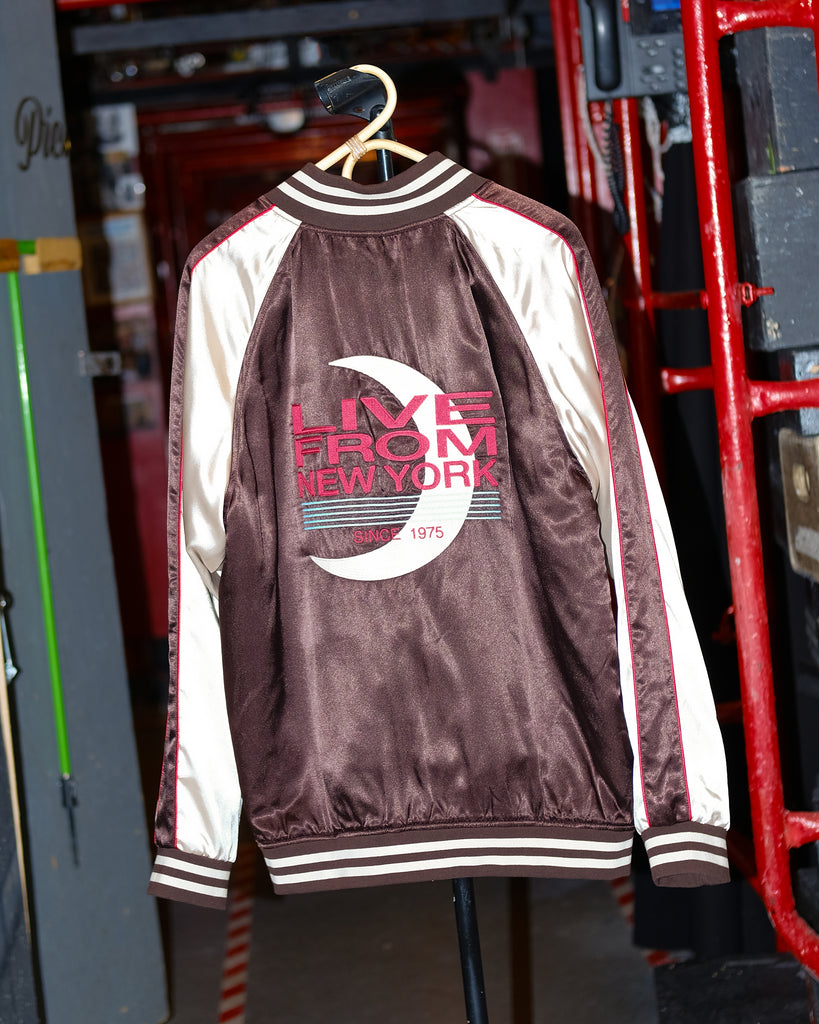Maroon and cream satin souvenir jacket with striped cuffs and collar. The back features a large embroidered design with a crescent moon and text reading 'Live From New York' and 'Since 1975' in red and teal.