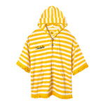 Yellow and white striped terrycloth poncho with short sleeves and yellow fringe trim. Features a hood with a tie closure, front pouch pocket, and black embroidered 'Tombolo' text on the chest.