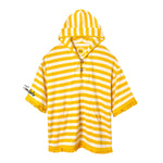 Yellow and white striped terrycloth poncho with short sleeves and yellow fringe trim. Features a hood with a tie closure, front pouch pocket, and black embroidered 'Tombolo' text on the sleeve.