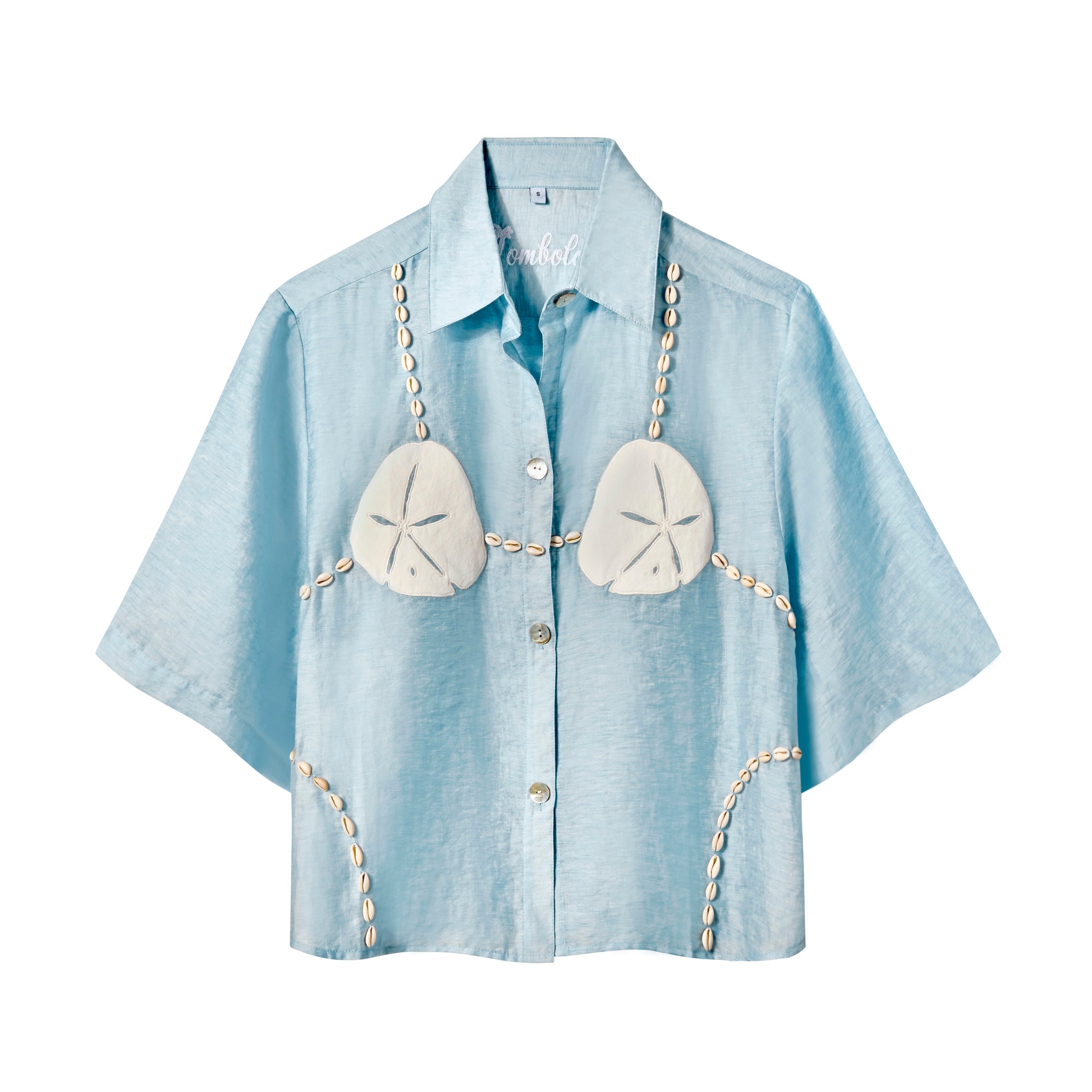Light blue, short-sleeve button-up shirt with a relaxed fit. The shirt features an embroidered design resembling a sand dollar bikini top, with two large cream-colored sand dollars at the chest and shell bead strands extending from the shoulders, across the chest, and down the sides.