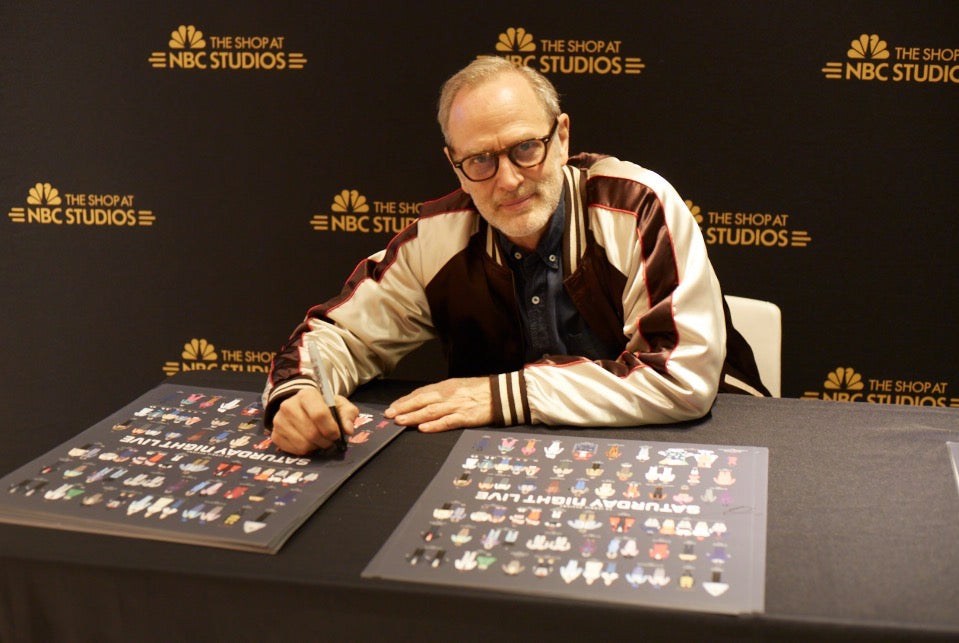 Tom Broecker signing SNL posters while wearing the SNL Souvenir Jacket. 