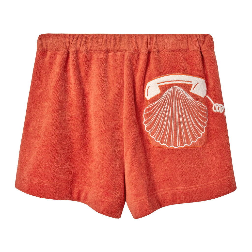 Back view of orange terry cloth shorts featuring a white embroidered rotary phone with a seashell design on the right side.