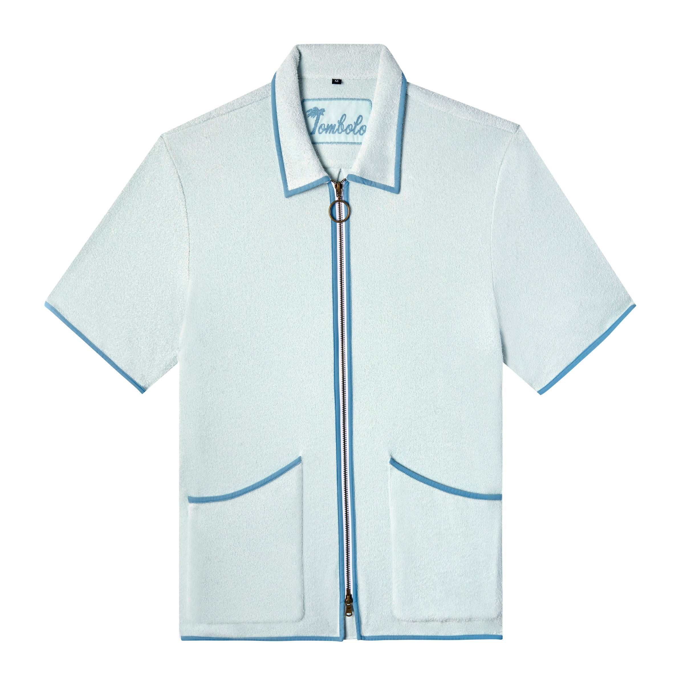 Front-facing product image of the 'Standard Issue' Cabana (Sky Blue) made of 100% Organic Terry Cloth with a two-way, antique-brass ring pull zipper, twin curved patch pockets, chain-stitched Tombolo interior label, and a 1/8" edge binding along collar, zipper, and pockets, all shot on a white background.