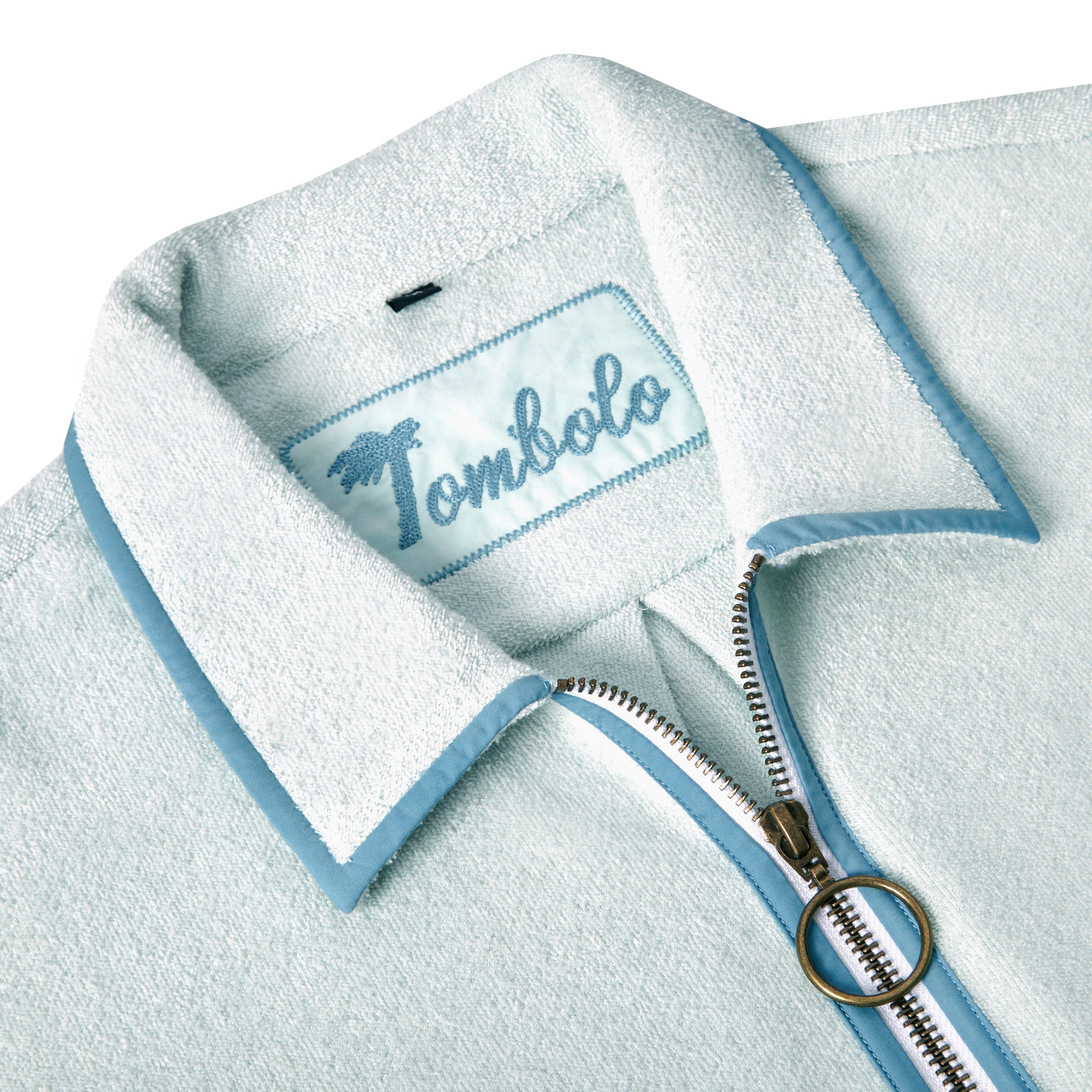 Close-up image of the 'Standard Issue' Cabana's (Sky Blue) interior chain-stitched label that says 'Tombolo,' and the antique brass two-way ring pull zipper. 