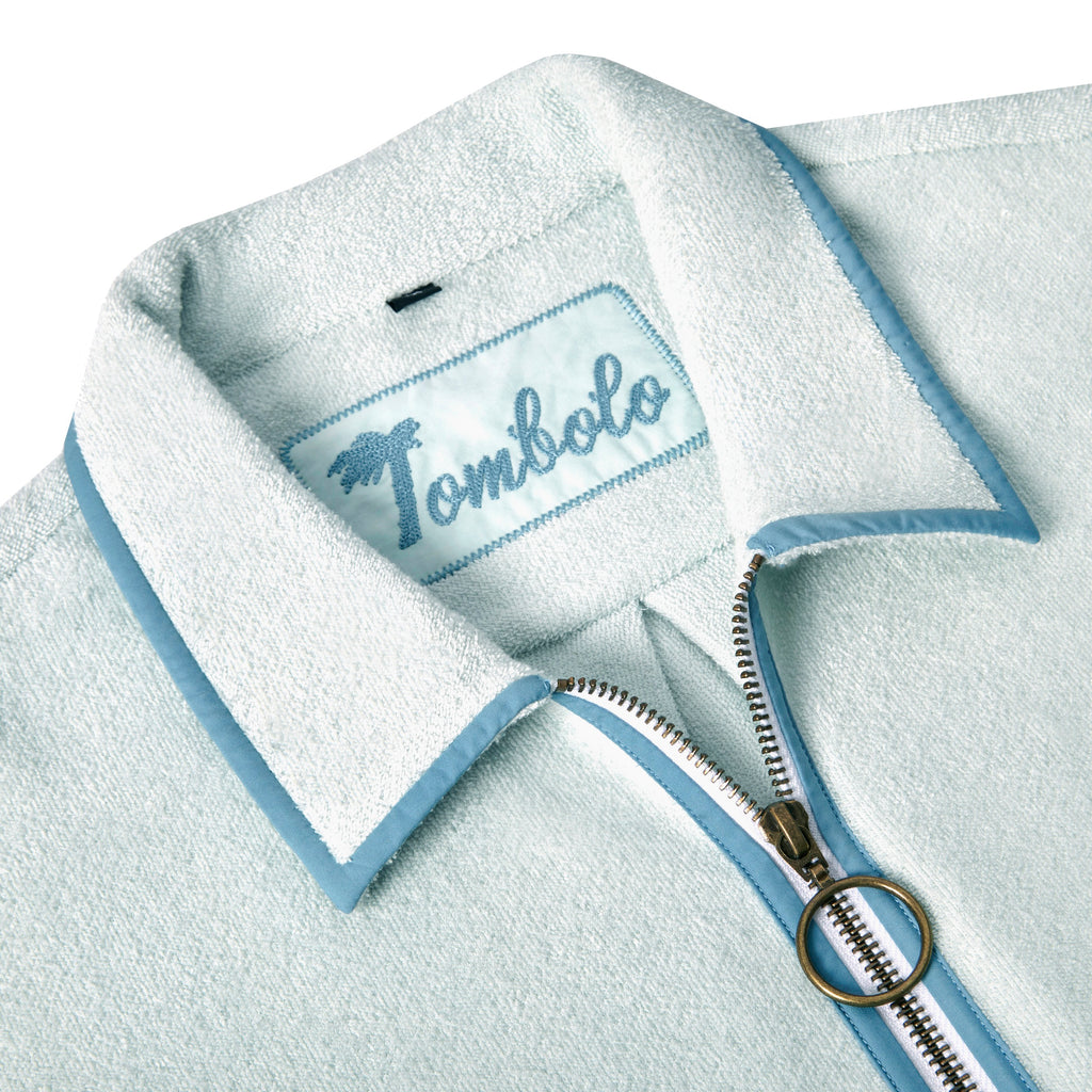 Close-up image of the 'Standard Issue' Cabana's (Sky Blue) interior chain-stitched label that says 'Tombolo,' and the antique brass two-way ring pull zipper. 