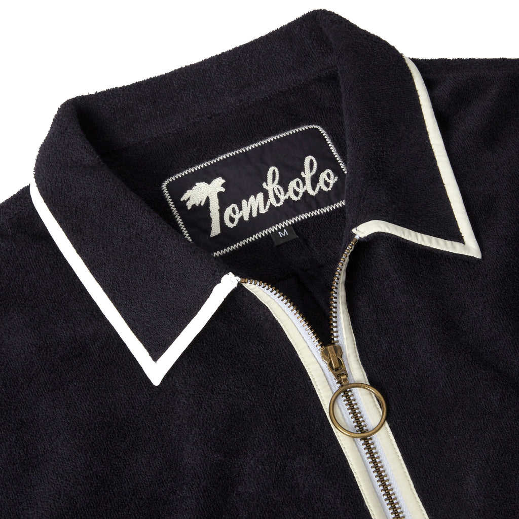 Close-up product image of the 'Standard Issue' Cabana's (Midnight Blue) chain-stitched interior logo that reads 'Tombolo,' and the garment's two-way, antique-brass ring pull zipper.