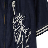 Close-up of white embroidered Statue of Liberty embroidery on navy cabana shirt, stitched along the front panel near the zipper.