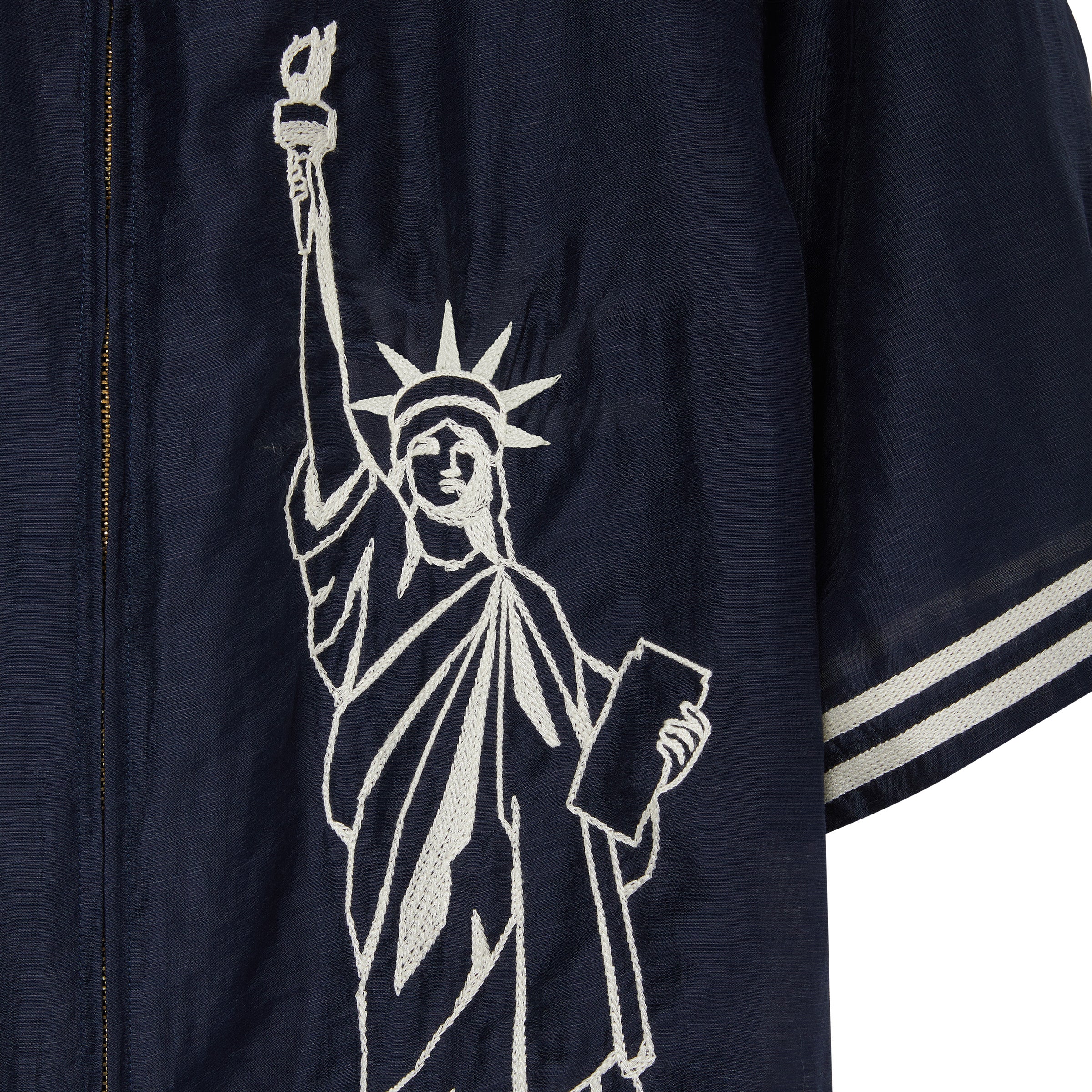 Close-up of white embroidered Statue of Liberty embroidery on navy cabana shirt, stitched along the front panel near the zipper.