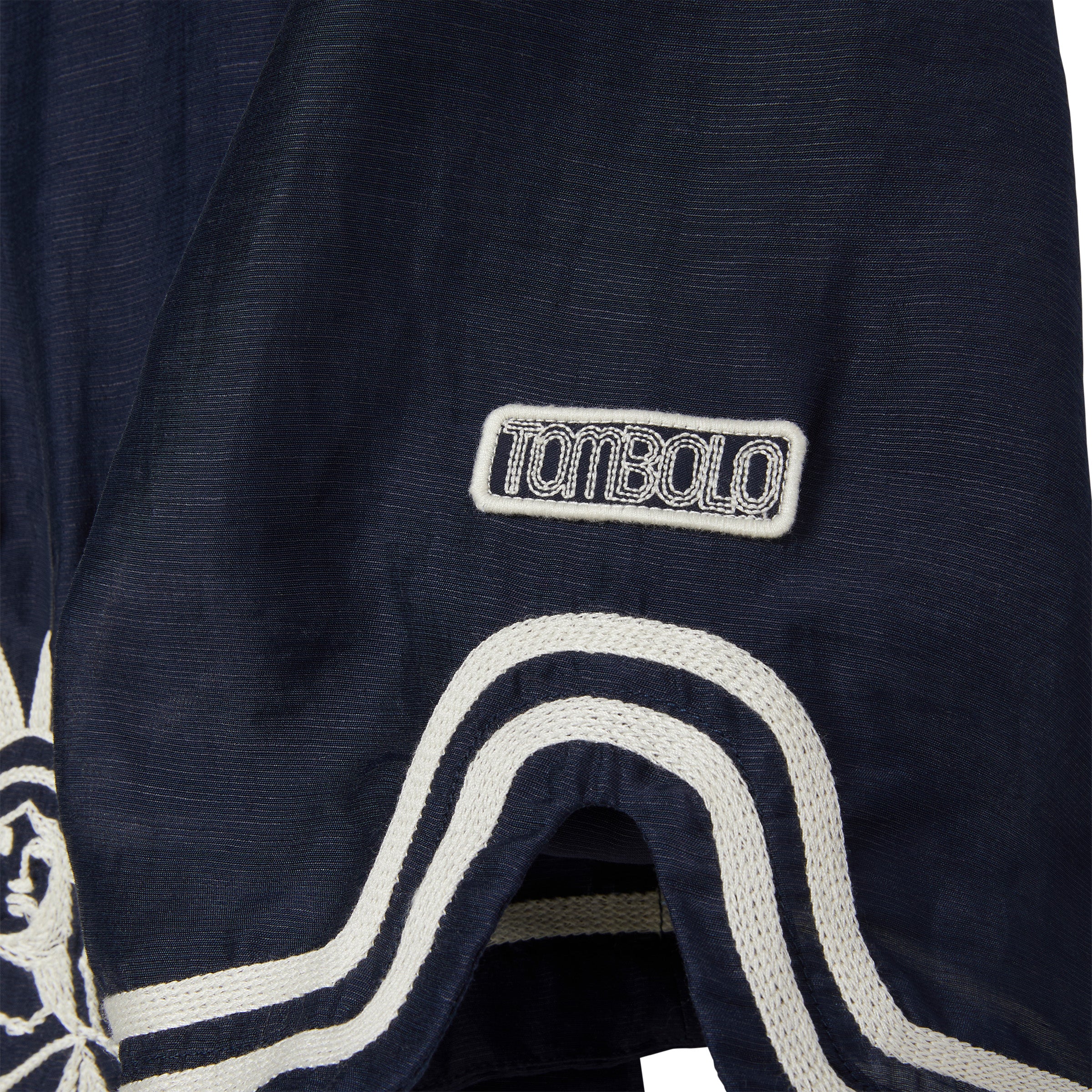 Navy blue shirt with white embroidery and white 'Tombolo' logo patch.