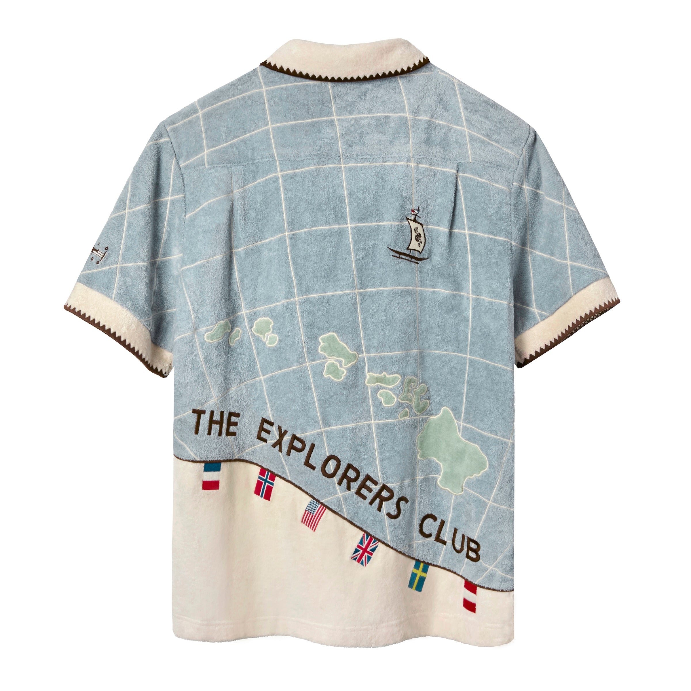 Back view of 'The Explorers Club' Expedition Cabana. The lower half is embroidered with green island shapes and the words "THE EXPLORERS CLUB" in brown lettering. A small sailboat is stitched near the upper right shoulder. The shirt’s hem includes colorful embroidered flags, and the collar and sleeve cuffs are finished with zigzag trim.