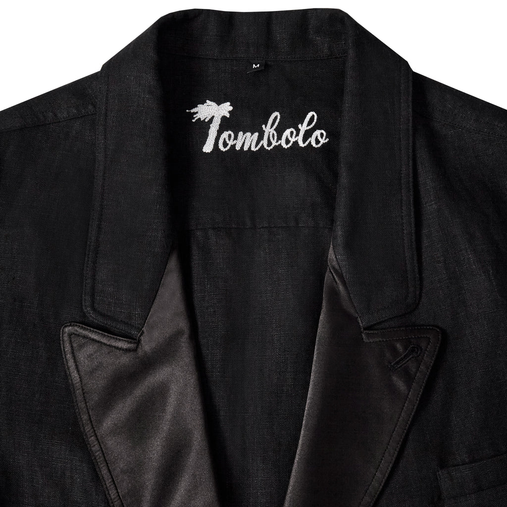 Close-up of a black jacket collar with satin lapel and embroidered 'Tombolo' logo inside the neckline.