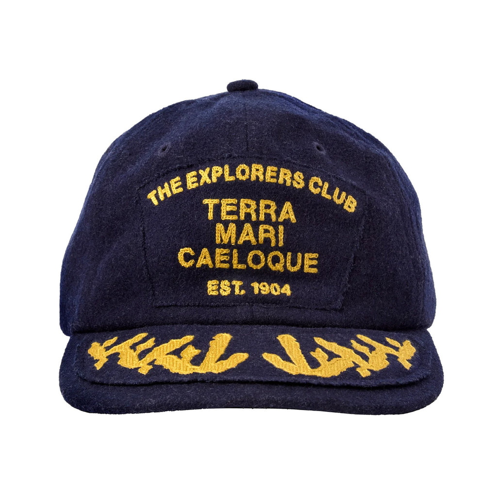 Navy wool baseball cap with gold embroidery. The front panel reads “THE EXPLORERS CLUB / TERRA MARI CAELOQUE / EST. 1904” in all caps. The brim features gold embroidered laurel-like detailing, giving the cap a vintage, nautical-inspired look.