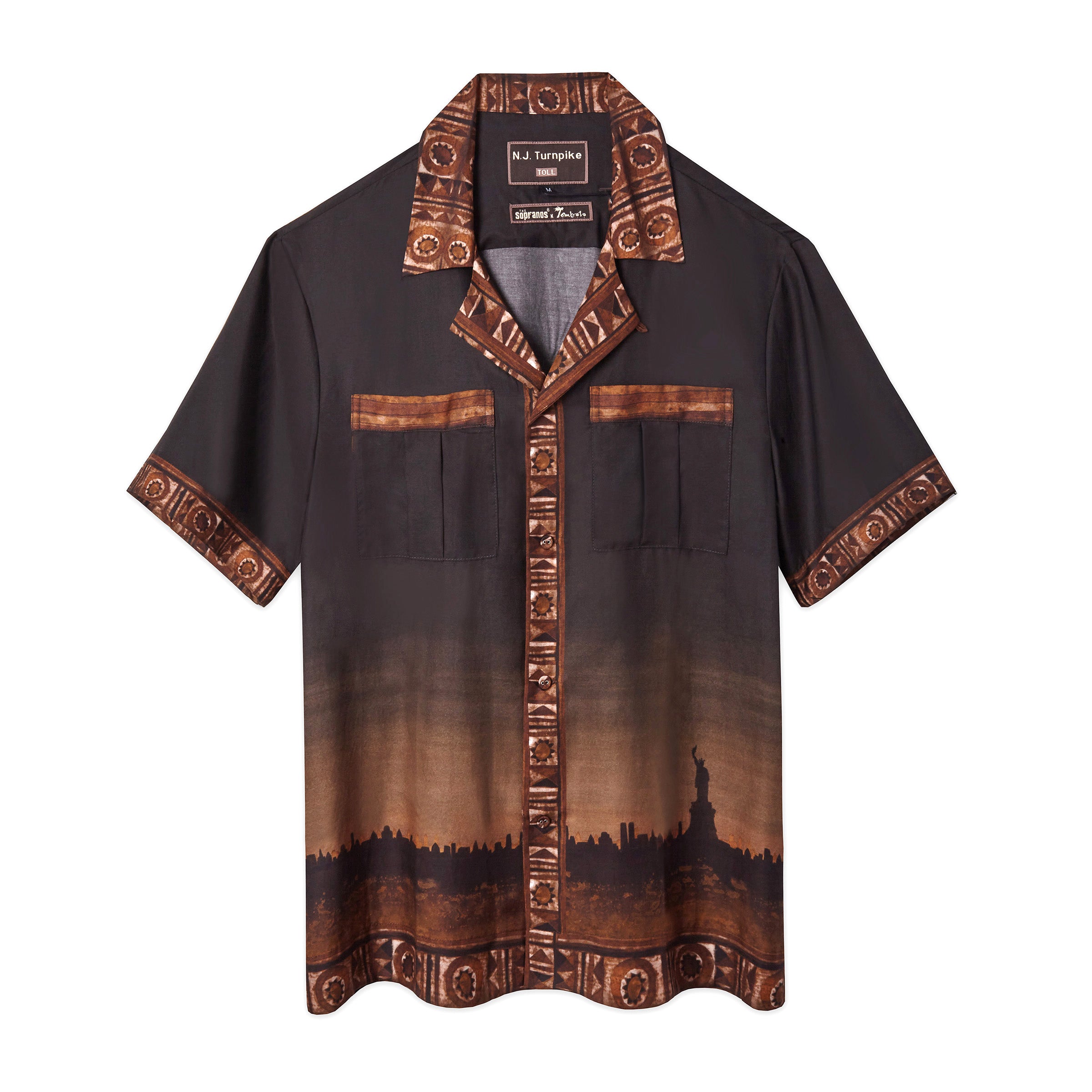 Front-facing product image of the 'The Sopranos' Turnpike Batik that features a digitally printed skyline of New York City including the Statue of Liberty, a custom woven 'The Sopranos' x Tombolo' collaboration label, and finally a contrasting batik collar, cuffs, placket, and bottom sweep, all of which exists on a brown gradient that resmebles a setting sun over the cityscape. Shot on a white background.