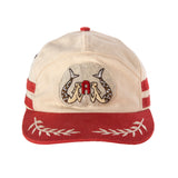 A beige and red 'Le Sirenuse' 7-Panel Souvenir Cap with hand-embroidered goldwork patch featuring Le Sirenuse, contrast brim and top button, and floral jacquard seam tape.